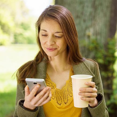 一个年轻女子在公园里悠闲地喝着咖啡，拿着手机看时事通讯
